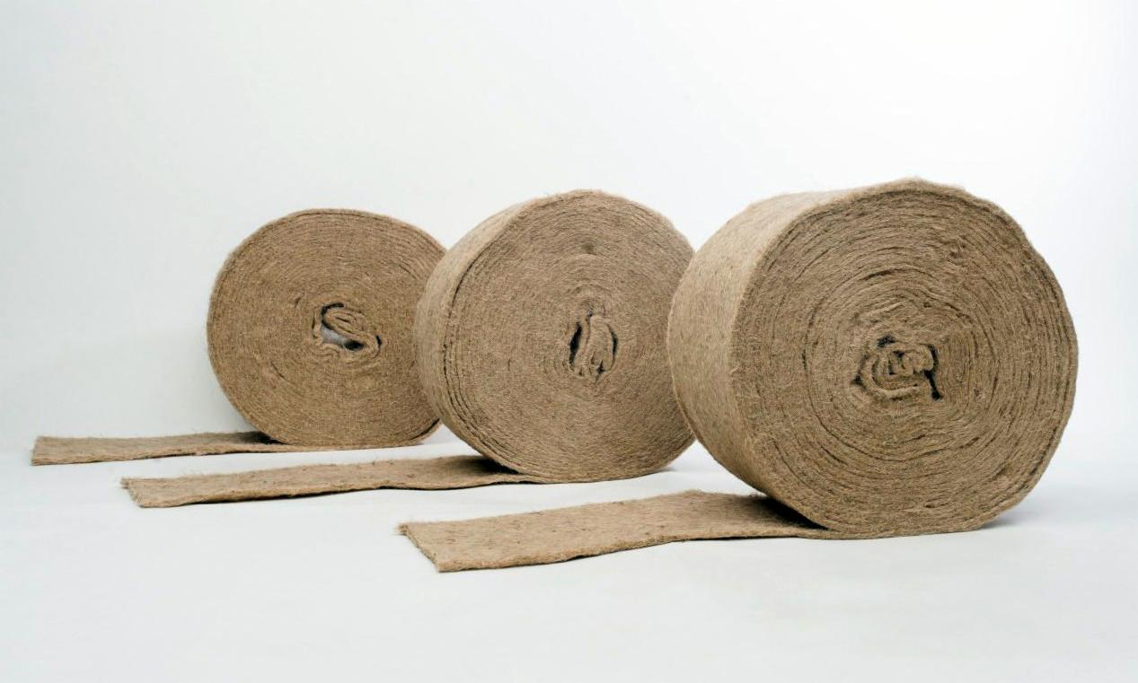Trzy rolki brązowej, naturalnej izolacji z lnu na białym tle, z widocznymi fragmentami rozwiniętej maty izolacyjnej.