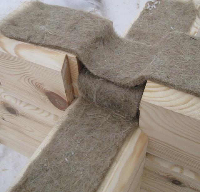 Fragment konstrukcji domu z bali, widoczne połączenie belek wypełnione naturalną izolacją z włókien roślinnych, surowe drewno jasne, widoczne słoje.