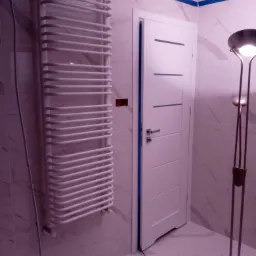 Nowoczesna łazienka z białymi płytkami imitującymi marmur, grzejnikiem drabinkowym, białą drzwiami z poziomymi frezami i lampą podłogową z okrągłym kloszem.