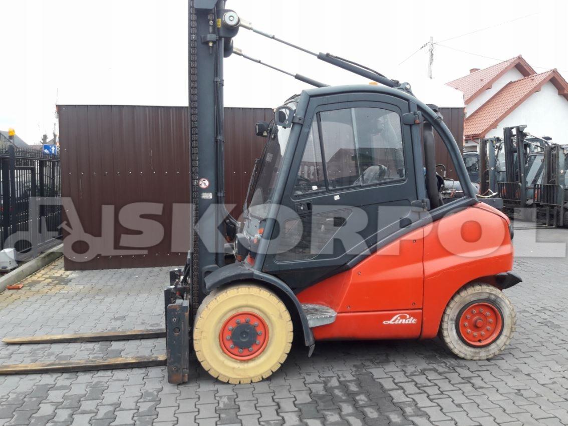 Pomarańczowo-czarny wózek widłowy marki Linde z żółtymi oponami na kostce brukowej, widoczne inne wózki w tle.