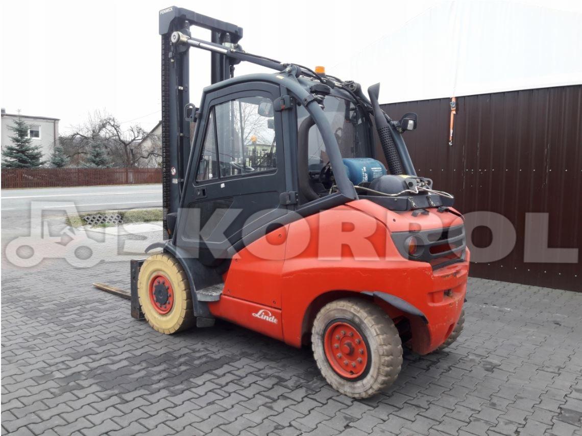 Pomarańczowo-czarny wózek widłowy marki Linde, stojący na kostce brukowej, z żółtymi oponami i widocznym zbiornikiem gazu.