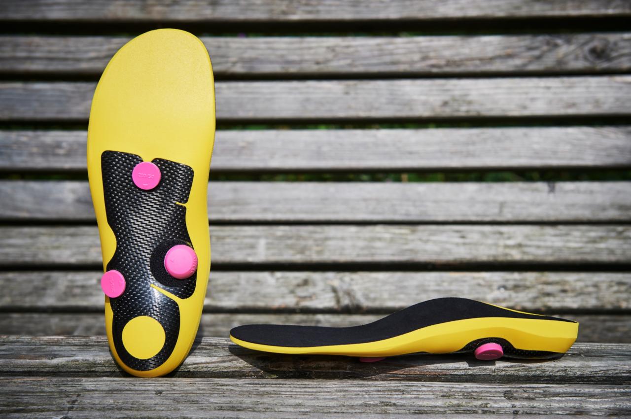 Żółto-czarne wkładki ortopedyczne z różowymi elementami na drewnianym tle, widok z boku i z góry.