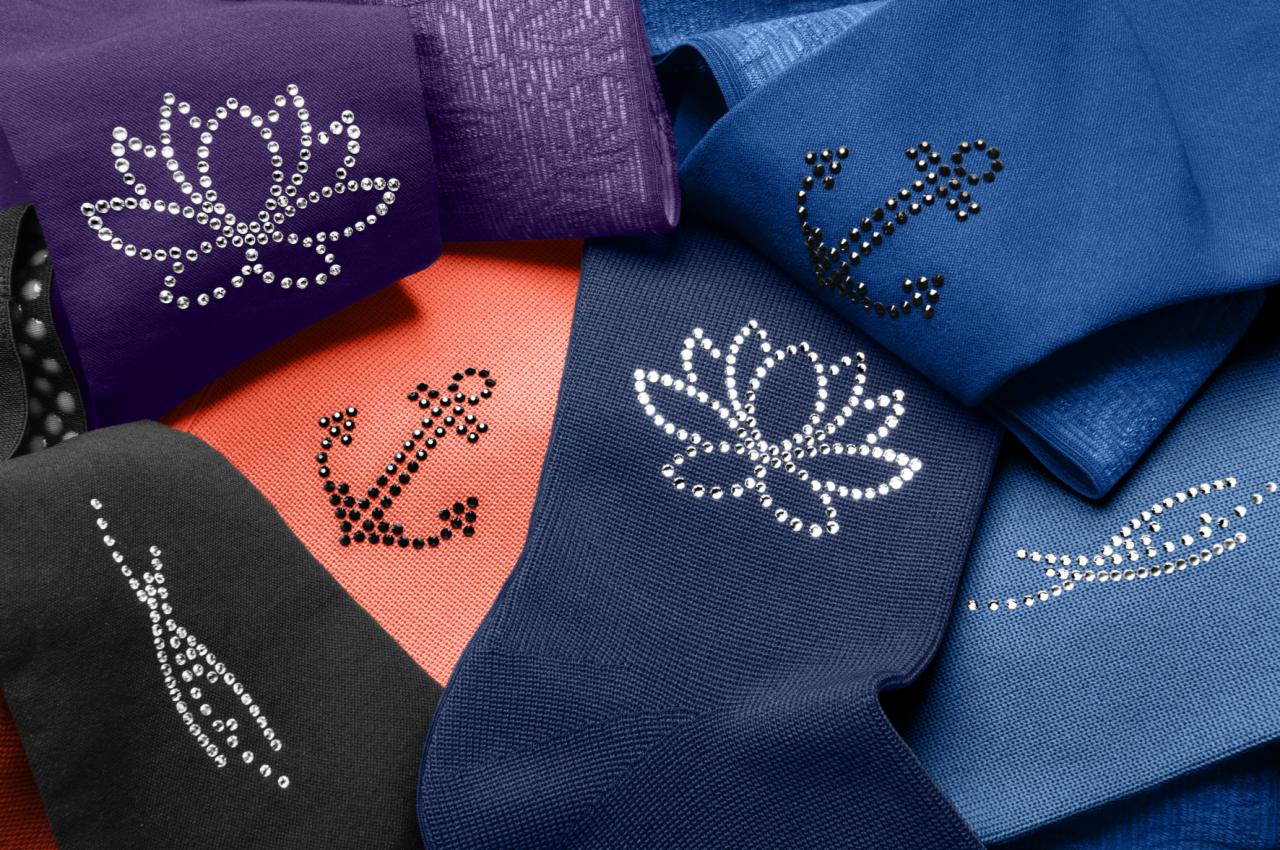 Kolorowe skarpetki z aplikacjami z dżetów w kształcie kwiatów lotosu, kotwicy i abstrakcyjnych wzorów, ułożone warstwami na płaskiej powierzchni.