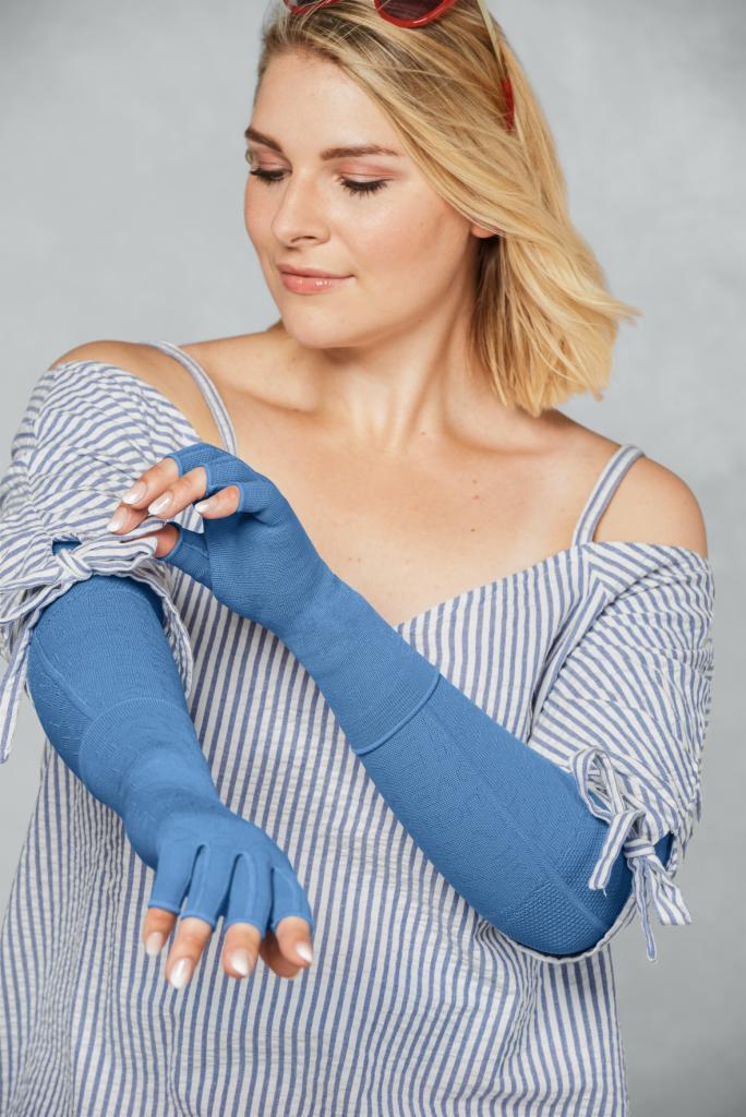 Kobieta w bluzce w paski prezentuje nałożone niebieskie rękawy uciskowe z otworami na palce.