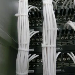 Zestawienie białych kabli zabezpieczonych opaskami zaciskowymi, podłączonych do urządzeń elektronicznych z licznymi portami BNC.