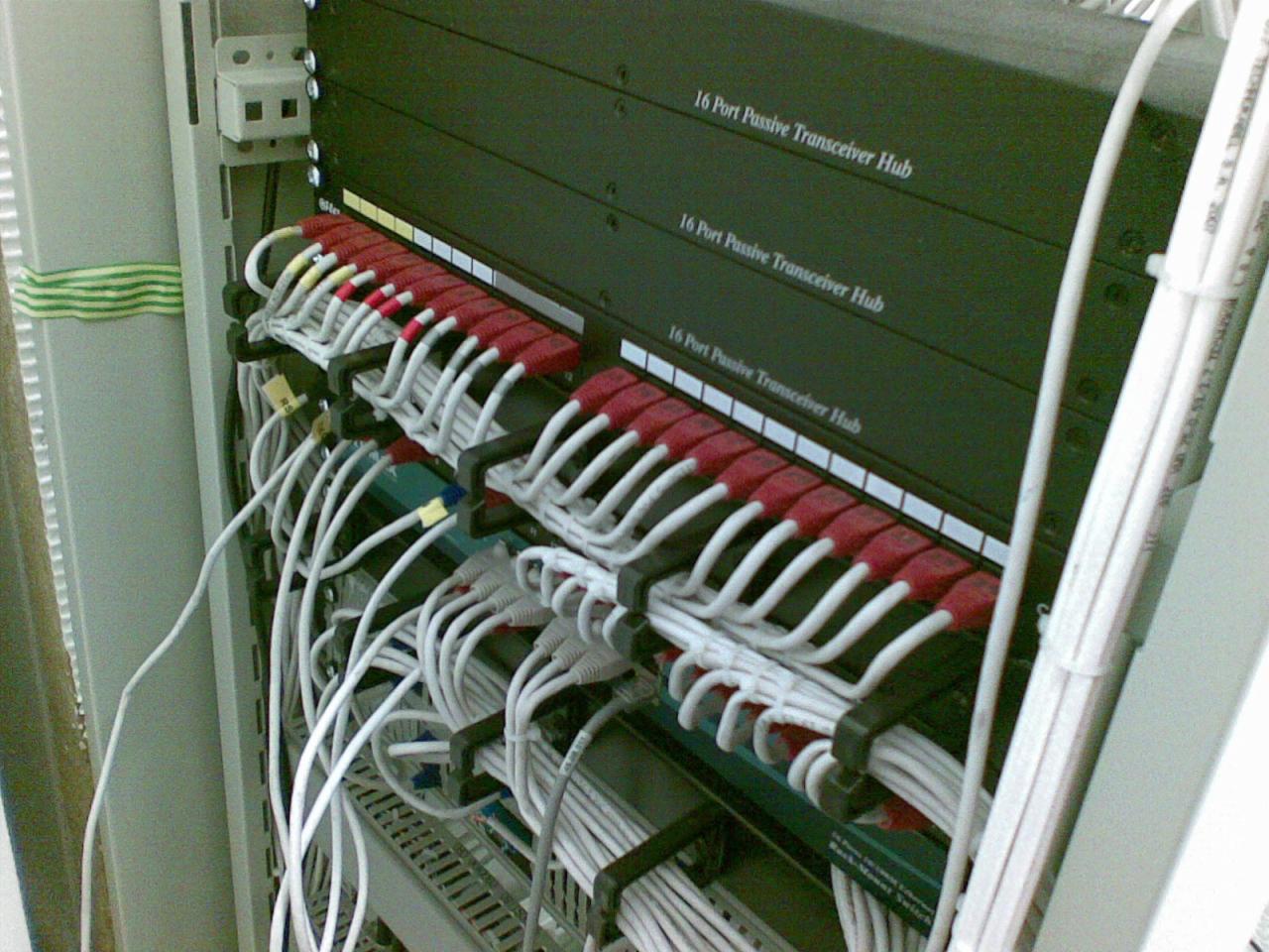 Szafa serwerowa z zainstalowanymi pasywnymi transceiverami 16-portowymi i uporządkowanymi kablami, widoczne oznaczenia portów i etykiety na kablach.