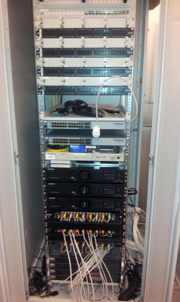 Szafa rack z zainstalowanymi urządzeniami sieciowymi, patch panele, switche ProCurve, okablowanie strukturalne w trakcie podłączania, widoczne kable zakończone wtykami RCA.