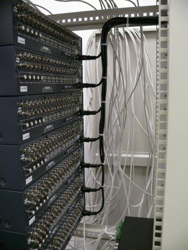 Serwerownia: Stojak z zamontowanymi urządzeniami sieciowymi, z licznymi kablami czarnymi i szarymi, uporządkowanymi za pomocą opasek zaciskowych.