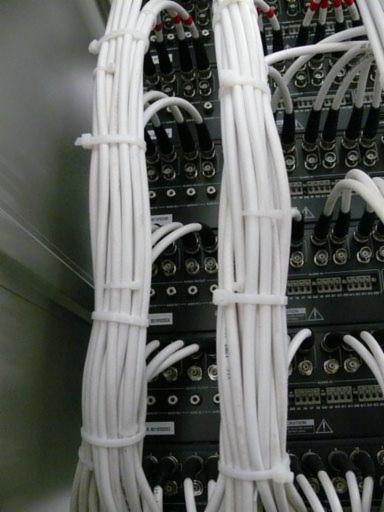 Zestawienie białych kabli zabezpieczonych opaskami zaciskowymi, podłączonych do urządzeń elektronicznych z licznymi portami BNC.