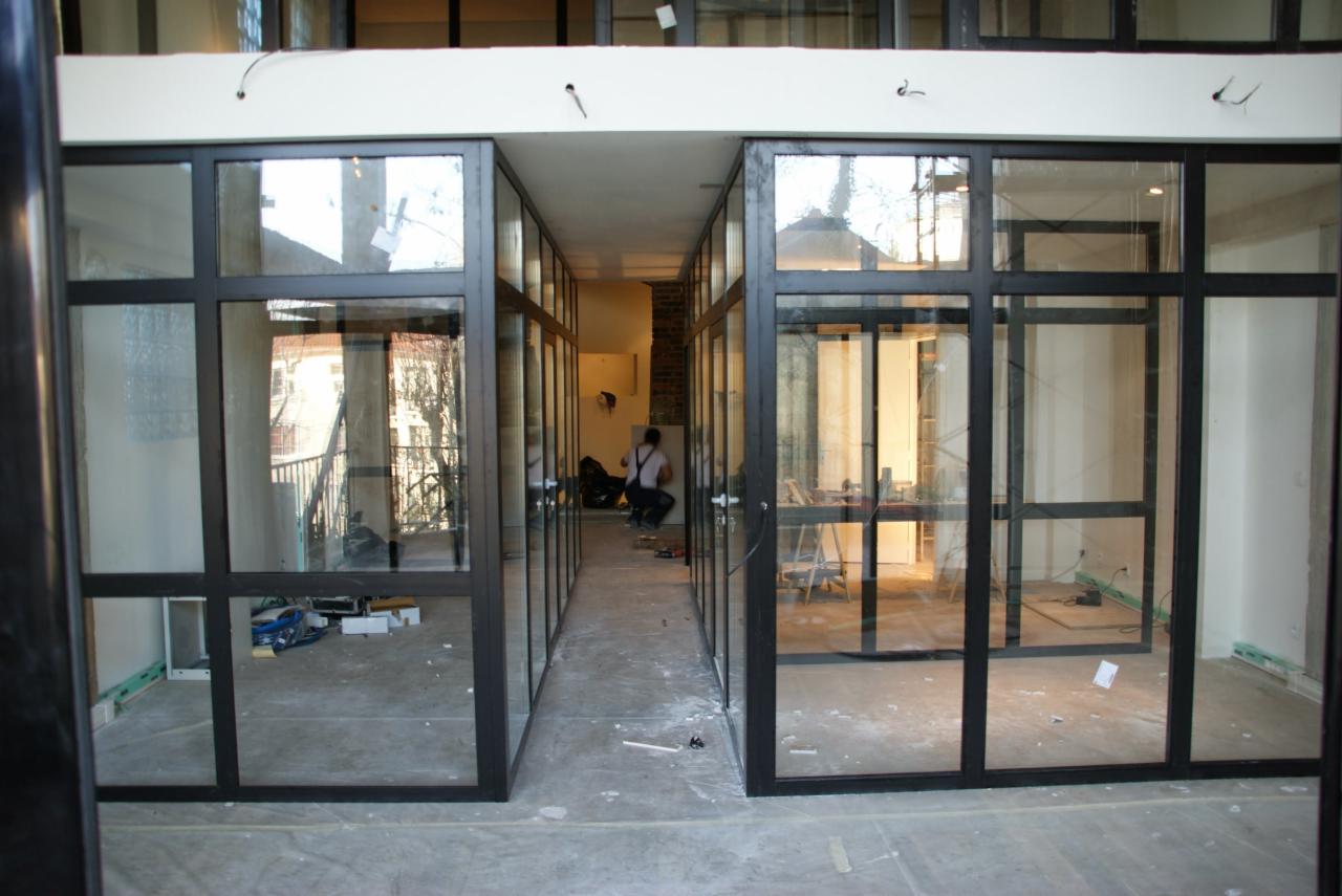 Montaż szklanych drzwi przesuwnych z czarnymi szprosami, widoczny pracownik w tle, surowy stan wykończenia.