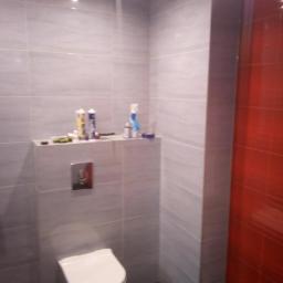 Osoba prywatna - Wykończona łazienka z szarymi płytkami na ścianach i czarną podłogą, widoczna toaleta i akcesoria łazienkowe na półce.