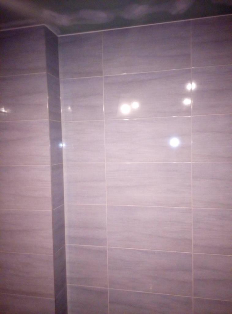 Ściana wyłożona błyszczącymi, szarymi płytkami ceramicznymi w łazience w Bytomiu, widoczny narożnik i fugi.