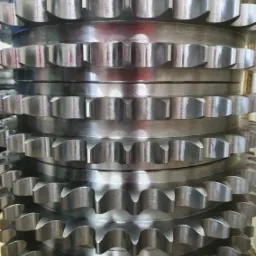 Stos metalowych kół łańcuchowych z precyzyjnie wyciętymi zębami, ułożonych jeden na drugim, ukazujących metaliczny połysk i dokładność wykonania.