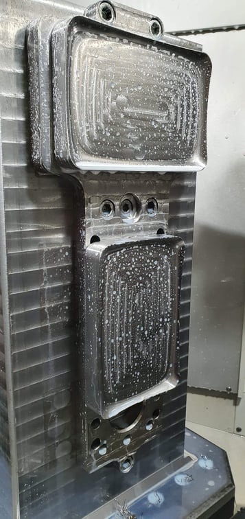 Obrabiany metalowy element z widocznymi śladami chłodziwa i frezowania, umieszczony w maszynie CNC.