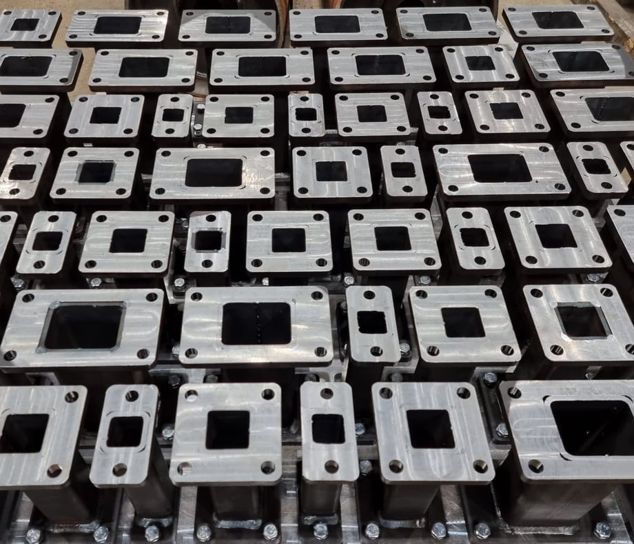 Równy rząd obrobionych metalowych elementów z otworami, ułożonych na metalowej powierzchni, widoczne ślady obróbki skrawaniem.