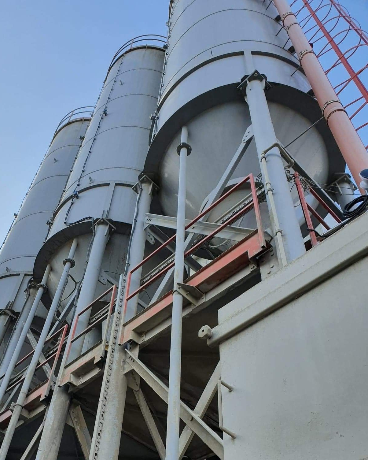 Silosy przemysłowe z metalową konstrukcją wsporczą, widoczne z dołu na tle błękitnego nieba w Radomiu.