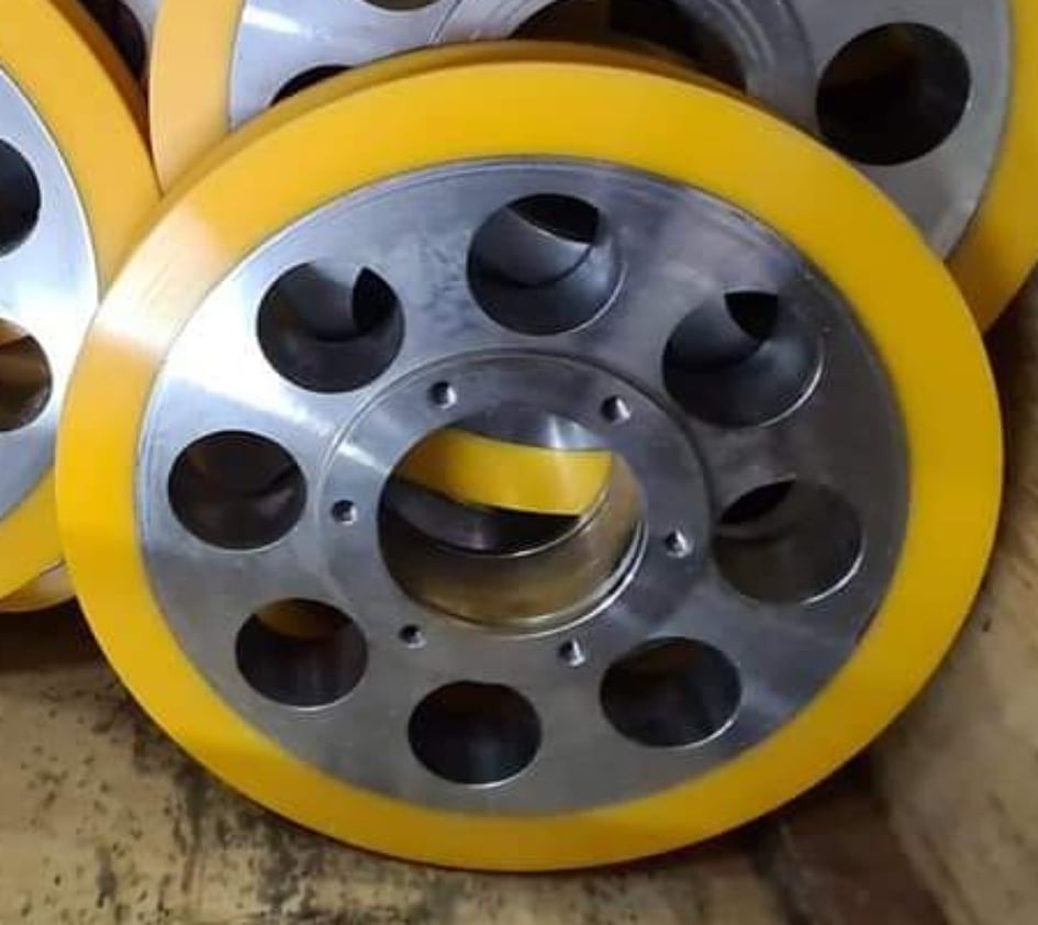 Metalowe koła z żółtą poliuretanową obwódką, widoczne otwory montażowe i odciążające, ułożone obok siebie.