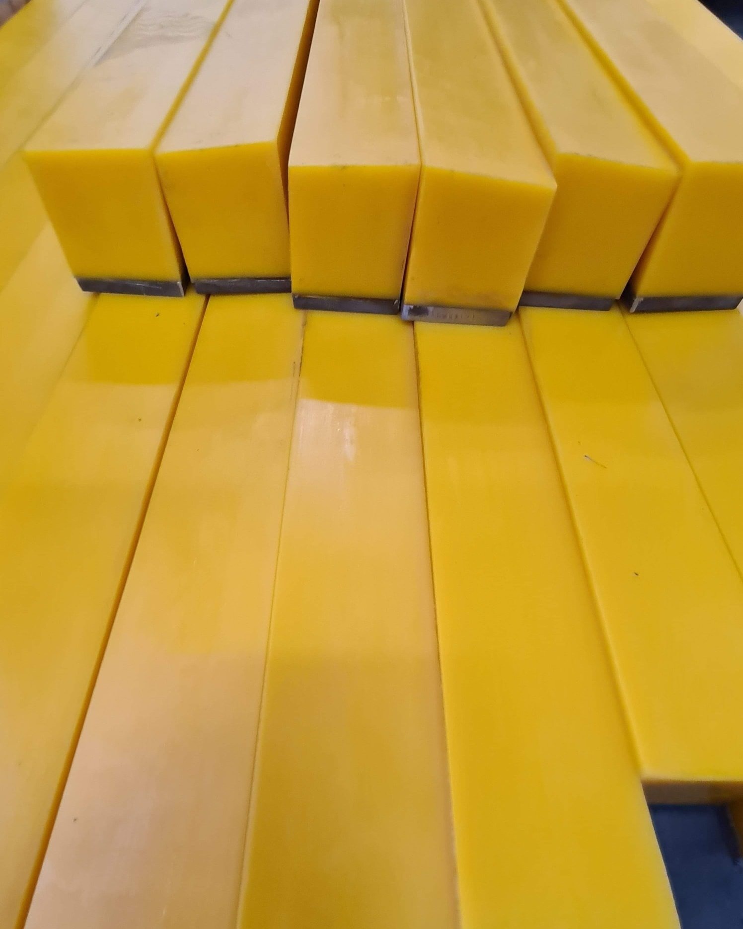 Żółte, prostokątne pręty z tworzywa sztucznego, ułożone jeden na drugim, z widocznymi śladami cięcia na końcach.
