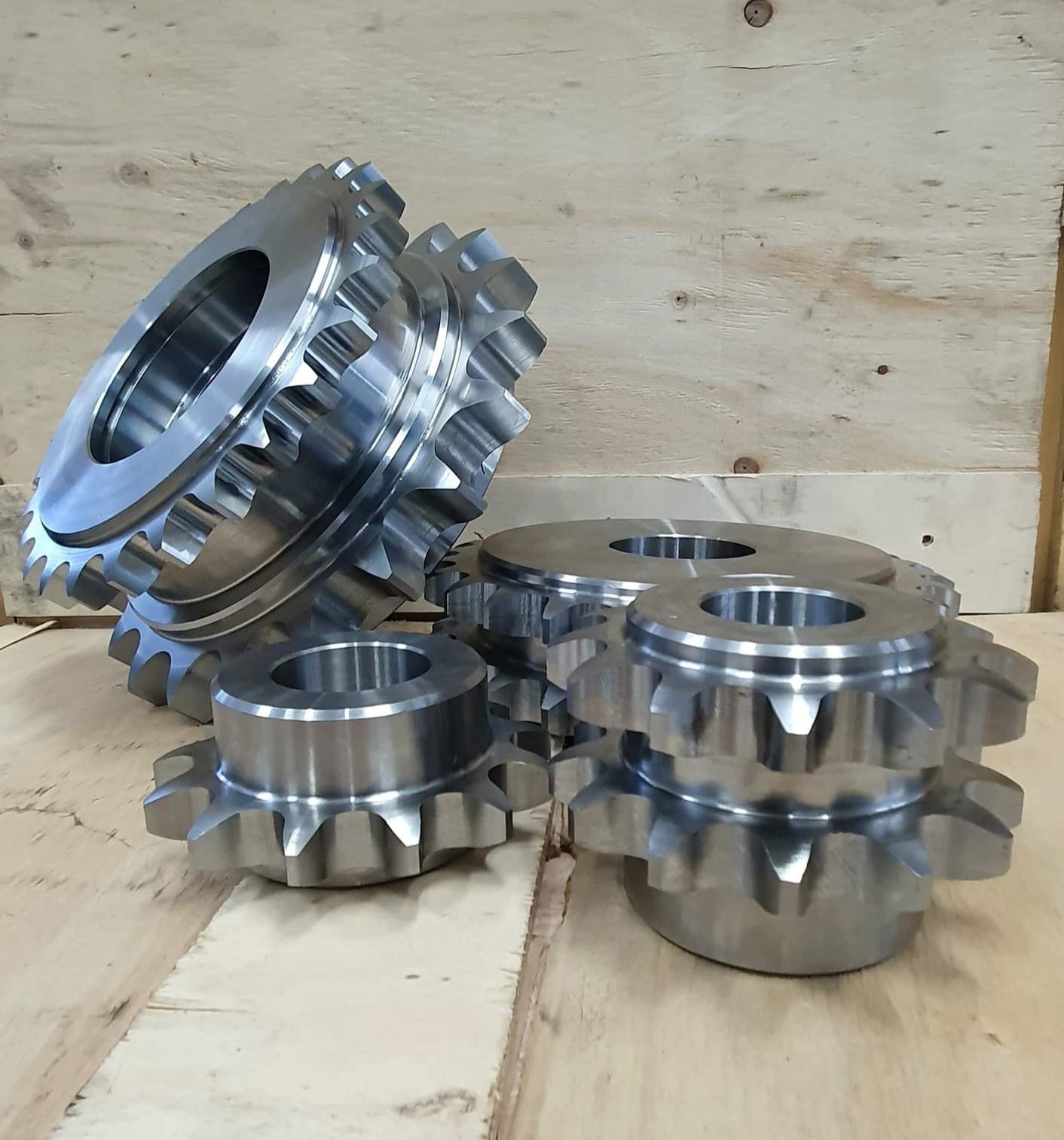 Stalowe koła zębate o różnej wielkości, leżące na drewnianej powierzchni na tle drewnianej ściany.