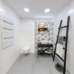 Nowoczesna łazienka w odcieniach bieli i szarości z dekoracyjną ścianą z wzorem chevron za umywalką, minimalistycznym grzejnikiem drabinkowym na ścianie i czarną, ozdobną drabiną z zawieszonymi...