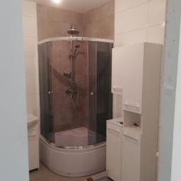 F.H.U Zając Robert - Ukończona łazienka z narożną kabiną prysznicową z brązowymi płytkami i białymi szafkami, widoczne ślady po remoncie na podłodze.