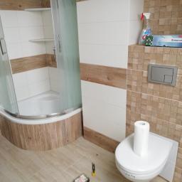 F.H.U Zając Robert - Nowoczesna łazienka po remoncie z kabiną prysznicową z zaokrąglonymi drzwiami, toaletą z rolką papieru i mozaiką na ścianach w odcieniach beżu i brązu.