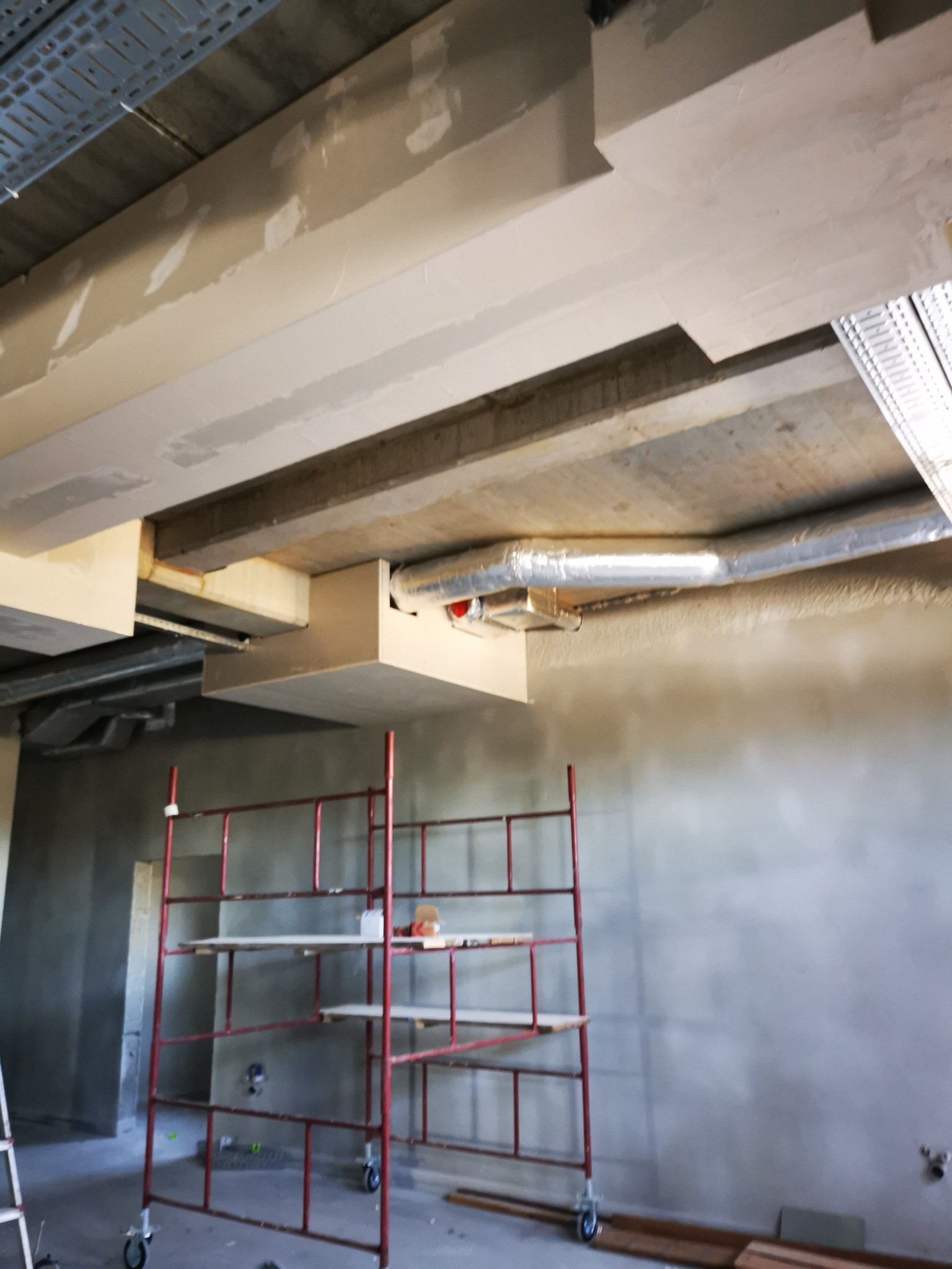 Sufit w trakcie wykańczania z widocznymi elementami konstrukcyjnymi, instalacjami i rusztowaniem malarskim.