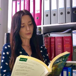 Kobieta w biurze czyta czasopismo prawnicze 'Palestra' na tle regału z segregatorami i komentarzami do kodeks&oacute;w.