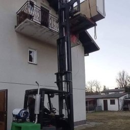 Mario-trans - Wózek widłowy Clark podnosi meble na balkon domu jednorodzinnego, widoczny operator w kabinie i butla gazowa na masce.