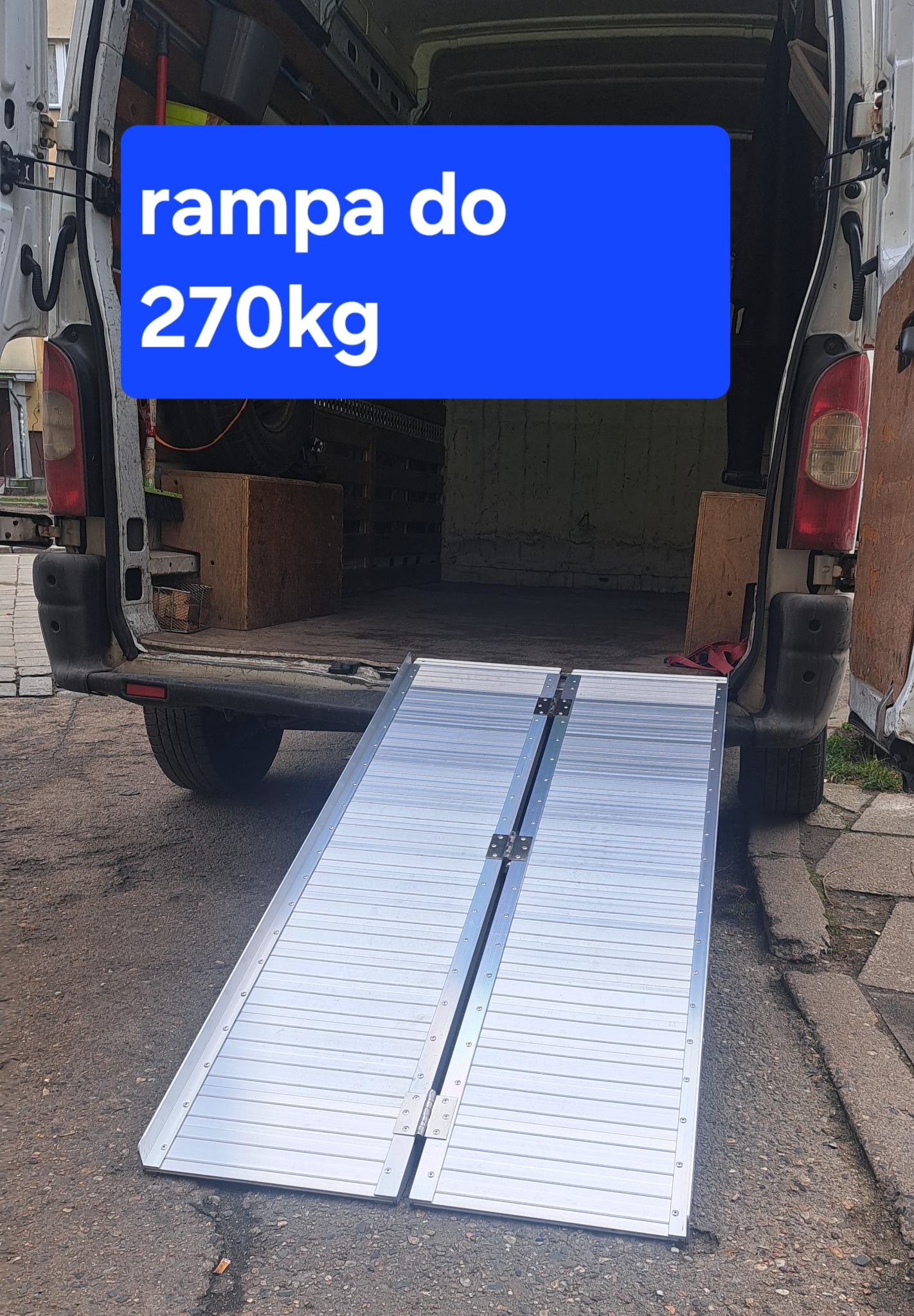 Rampa najazdowa do 270 kg, rozłożona przy tylnych drzwiach busa. Ułatwienie załadunku towarów. Widok z zewnątrz.