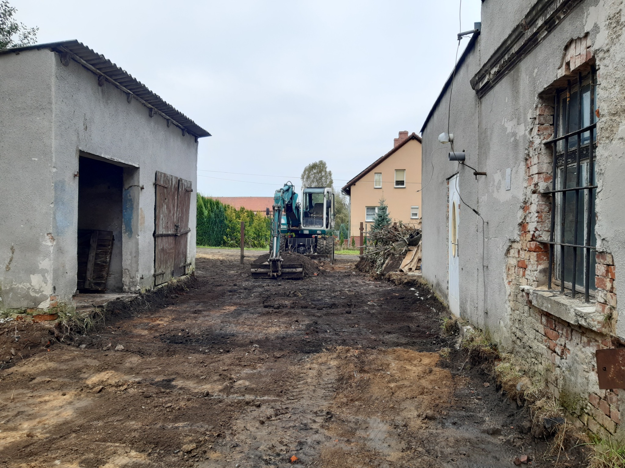 Mała koparka na placu budowy pomiędzy starymi budynkami, przygotowanie terenu pod prace ziemne.