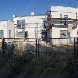 Intimo - Dwukondygnacyjny budynek z płaskim dachem w trakcie remontu elewacji, widoczne rusztowania, okna zabezpieczone folią, teren ogrodzony metalową siatką.