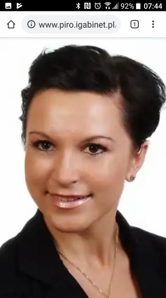 Portret kobiety z krótkimi, ciemnymi włosami, delikatnym makijażem i subtelną biżuterią, uśmiechająca się do kamery.