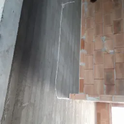 Surowa ściana z cegły z poprowadzonymi przewodami elektrycznymi, widoczne puszki instalacyjne i przewody wystające ze ściany, obok surowy beton.