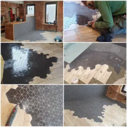 Układanie heksagonalnych, grafitowych płytek z geometrycznym wzorem na podłodze, w części pomieszczenia widoczne drewnopodobne panele, glazurnik docina płytki szlifierką kątową, widoczne narzędzia...