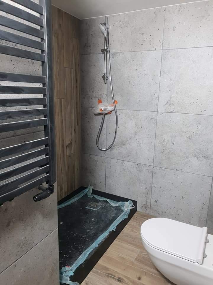 Montaż kabiny prysznicowej z odpływem liniowym i grzejnika drabinkowego w łazience w Świnoujściu, zabezpieczone folią ochronną przed zabrudzeniem podczas dalszych prac.