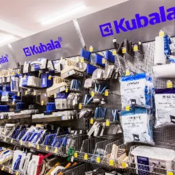 Półki w sklepie budowlanym w Rzeszowie, wypełnione narzędziami marki Kubala, w tym różnego rodzaju szpachelki, pędzle, wałki i akcesoria do tynkowania i malowania.