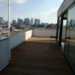 Biuro na dachu z drewnianym tarasem, widok na panoramę miasta w tle, krzesła składane i przesuwne szklane drzwi.