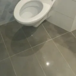 Nowoczesna toaleta z szarą podłogą i ścianami wyłożonymi płytkami w geometryczne wzory, widoczne białe fugi.