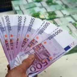 Dłoń trzymająca wachlarz banknotów 500 euro na rozmytym tle stosów banknotów.