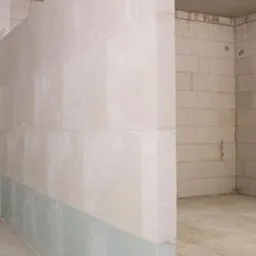 Świeżo wymurowana ściana działowa z betonu komórkowego, zabezpieczona folią ochronną u dołu, w surowym stanie deweloperskim.