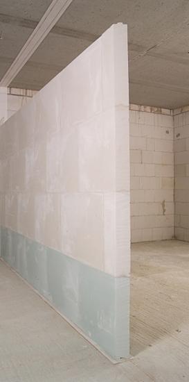 Świeżo wymurowana ściana działowa z betonu komórkowego, zabezpieczona folią ochronną u dołu, w surowym stanie deweloperskim.