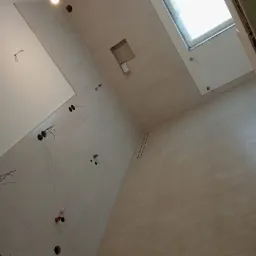 Łazienka w trakcie remontu z beżowymi płytkami, widoczne otwory na instalacje, surowy sufit z oknem dachowym i wystającymi przewodami elektrycznymi.