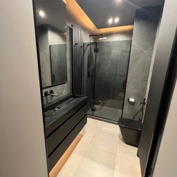DOM4YOU - Nowoczesna łazienka w odcieniach szarości i czerni z minimalistyczną umywalką na szafce z podświetleniem LED, kabiną prysznicową typu walk-in i wiszącą toaletą.