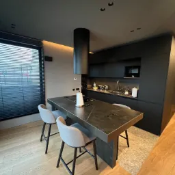 Nowoczesna kuchnia w odcieniach szarości i czerni z wyspą z blatem imitującym marmur, minimalistycznym okapem i drewnianą podłogą.