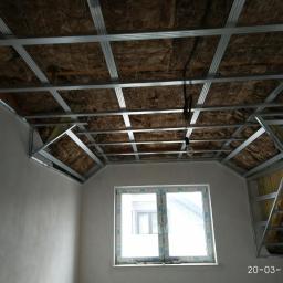 DOM4YOU - Montaż metalowej konstrukcji sufitu podwieszanego z izolacją z wełny mineralnej na poddaszu, widoczne profile i okno.