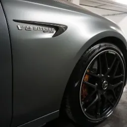 Matowy, szary samochód z czarnymi felgami i napisem V8 BITURBO 4MATIC na błotniku, widok z bliska na przednie koło i fragment karoserii.