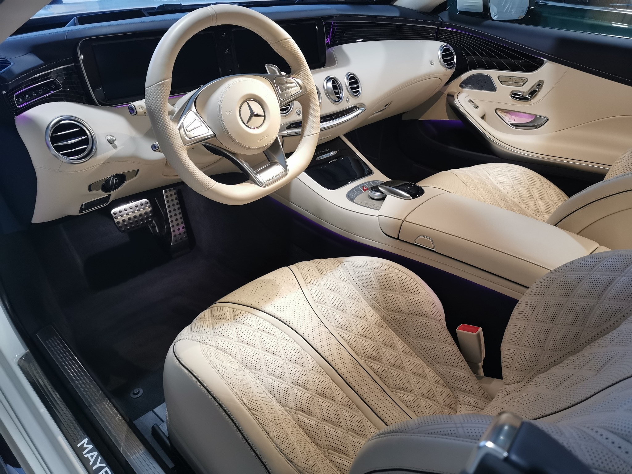 Wnętrze luksusowego samochodu Maybach w Kielcach, z jasną skórzaną tapicerką w romby, widoczna deska rozdzielcza, kierownica z logo Mercedes i pedały ze stali nierdzewnej.