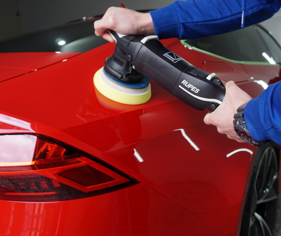 Polerowanie czerwonego lakieru samochodu maszyną polerską Rupes, widoczny odbijający się blask na karoserii i fragment tylnej lampy.