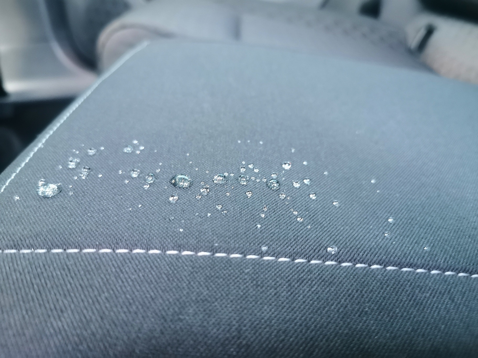 Szare siedzisko samochodowe z widocznymi kroplami wody po impregnacji, z bliska, szew z białej nici.